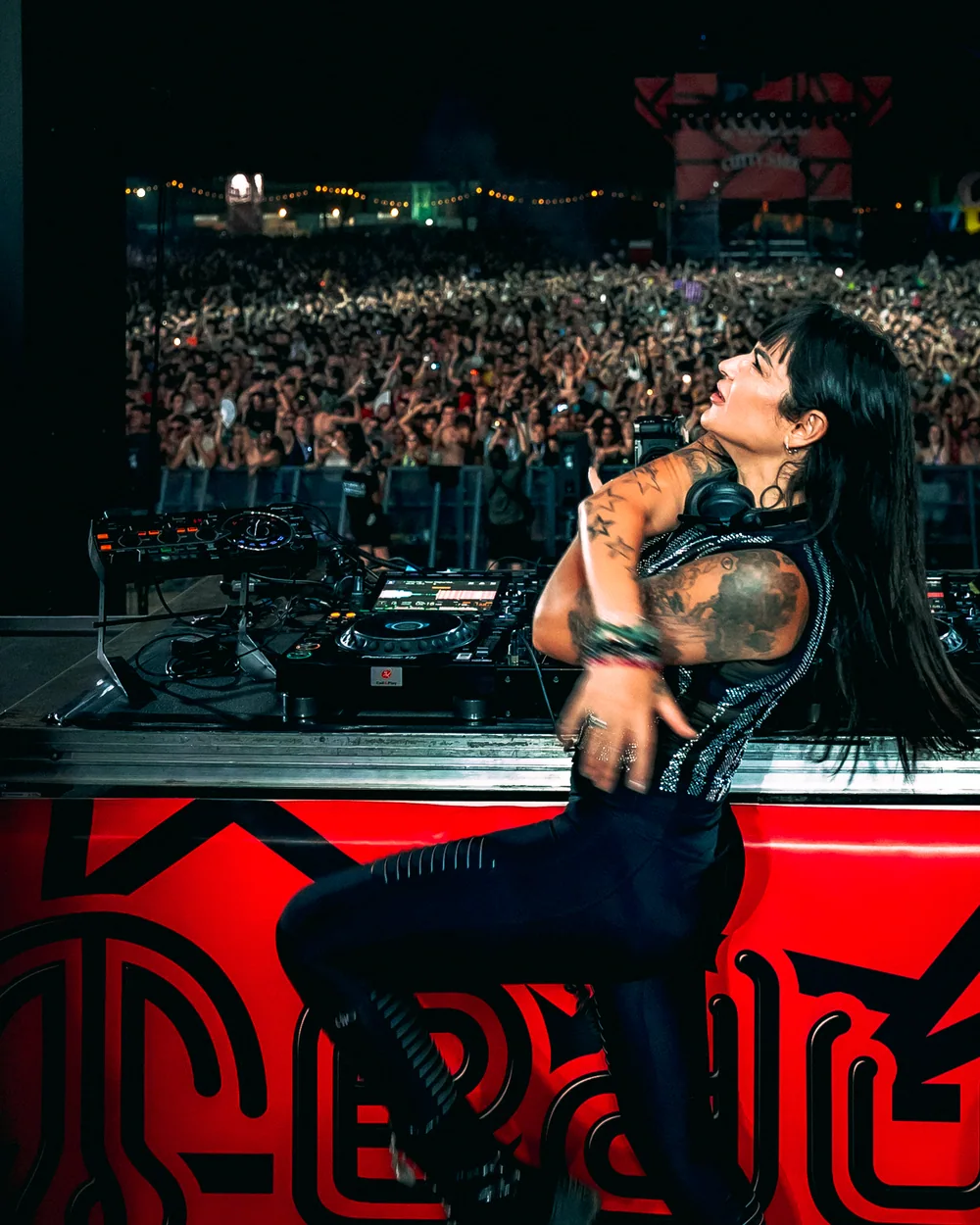 Fátima seated beside the decks, looking up, with the crowd behind her
